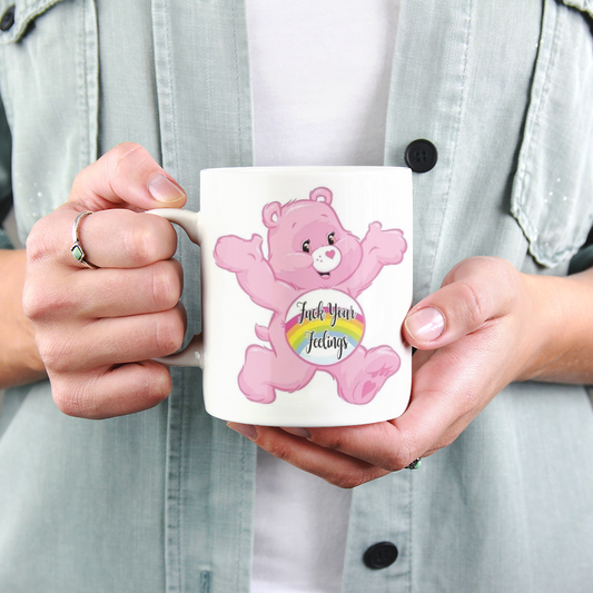Person holding a mug with a pink bear design and text "f*ck your feelings".