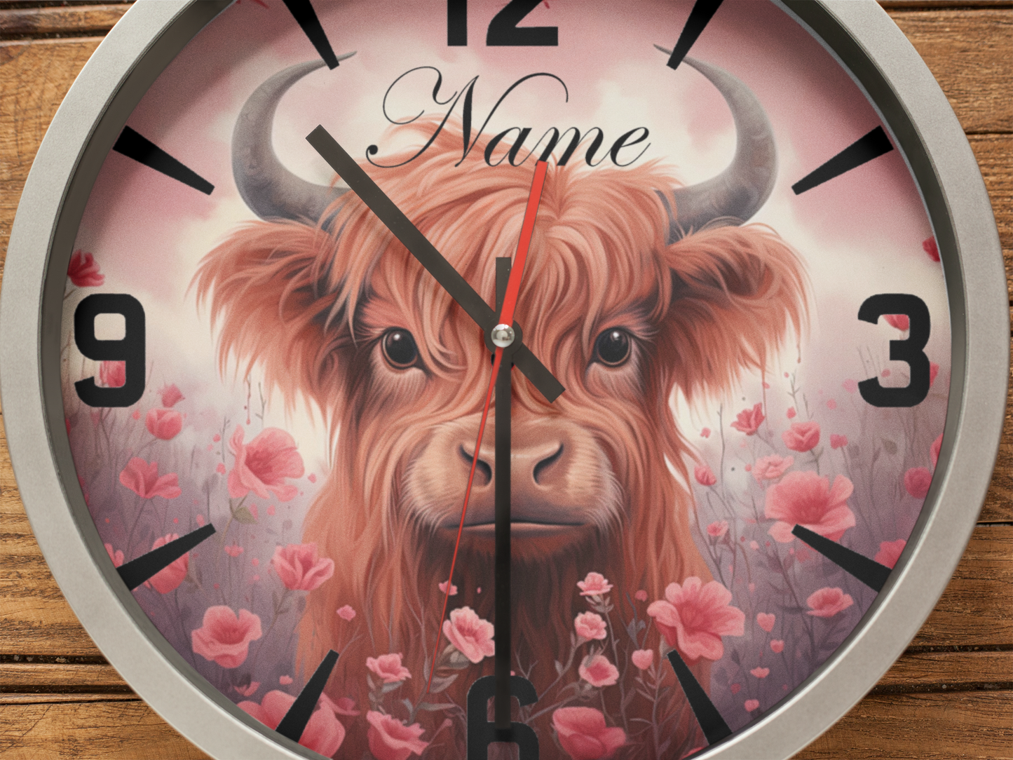 Closeup view of Silver Metal Wall clock featuring an image of a highland cow and the text: "name" on a wooden background