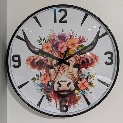 Wall clock with a decorative design of a highland cow's face surrounded by flowers on a white background.