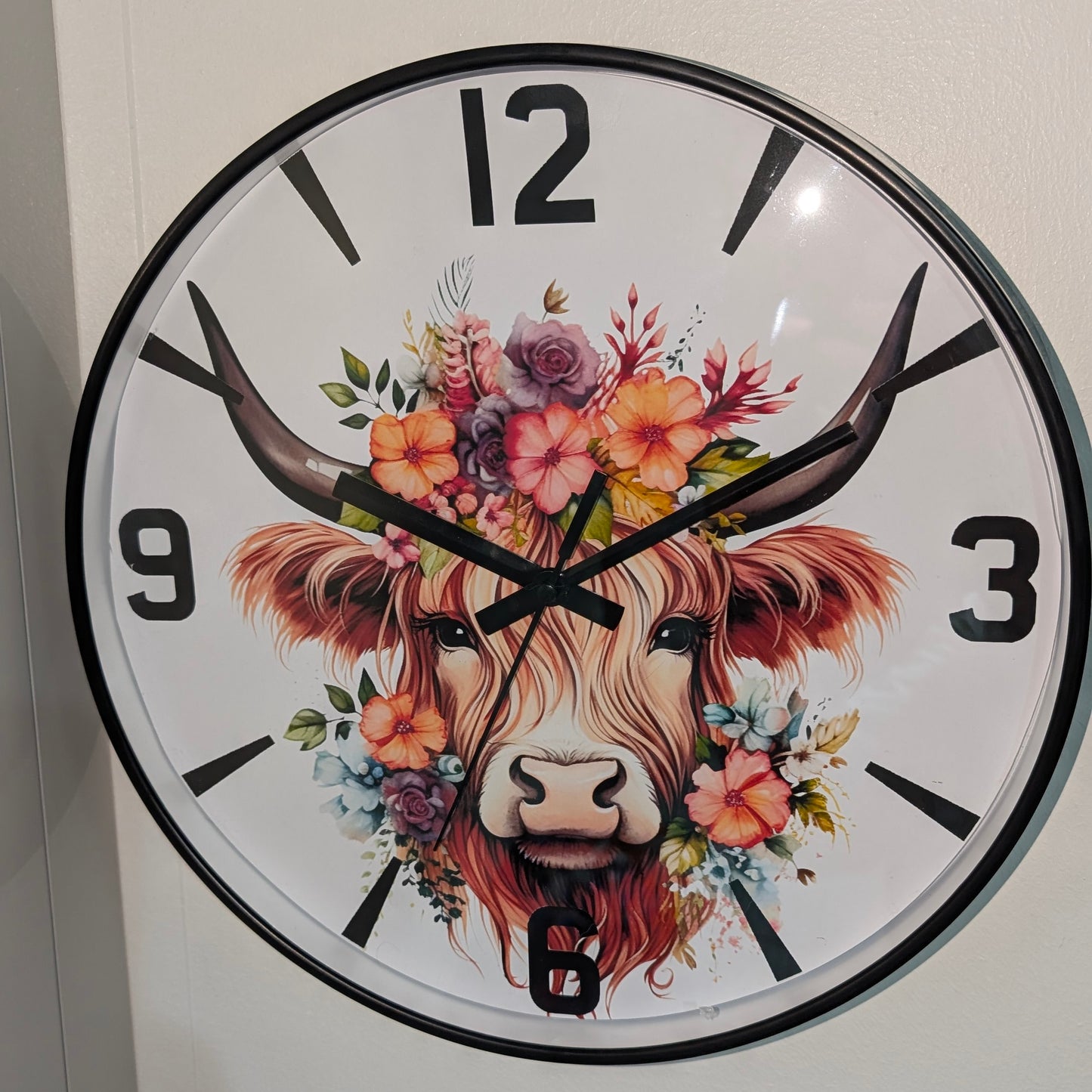 Wall clock with a decorative design of a cow's face and floral horns on a white background.