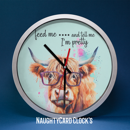 A wall clock featuring an illustration of a Highland cow with glasses, with a caption 'feed me... and tell me I'm pretty'.