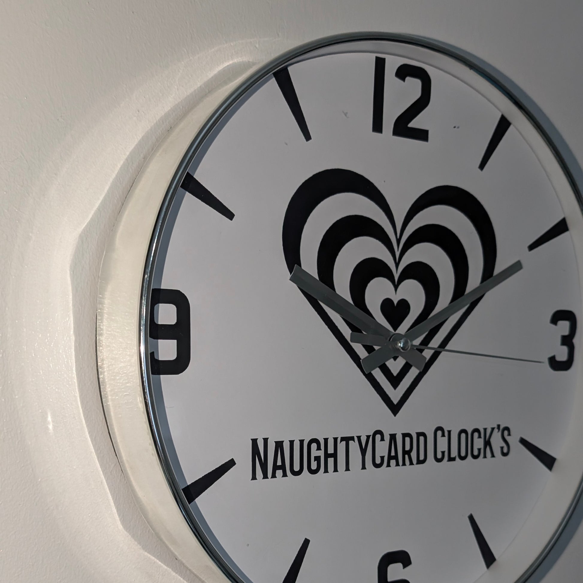 Silver Wall clock with heart design and 'NAUGHTYCARD CLOCK'S' text on a white background
