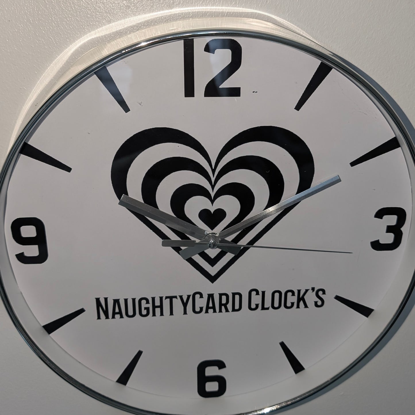 Wall clock with heart design and 'NaughtyCard Clock's' branding on a white background