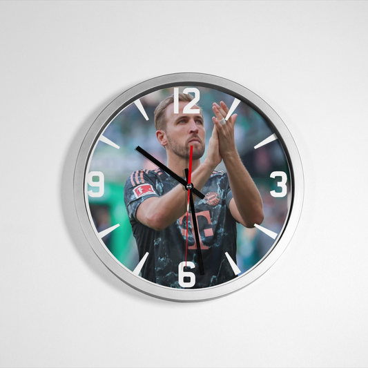 A wall clock featuring an image of Harry Kane with a playful expression, predominantly in black and white with a silver or metallic accent. Wall Clock from NaughtyCard