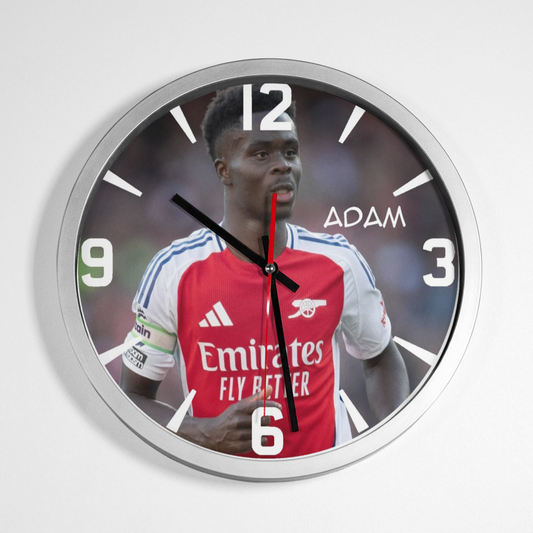 A wall clock featuring an image of Bukayo Saka wearing a football kit with the text 'Emirates FLY BETTER' on it, with clock hands and numbers in a visible part of the image.